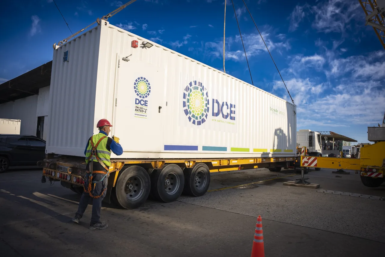 Módulo contenedor de DCE suspendido con grúa sobre un camión durante su traslado